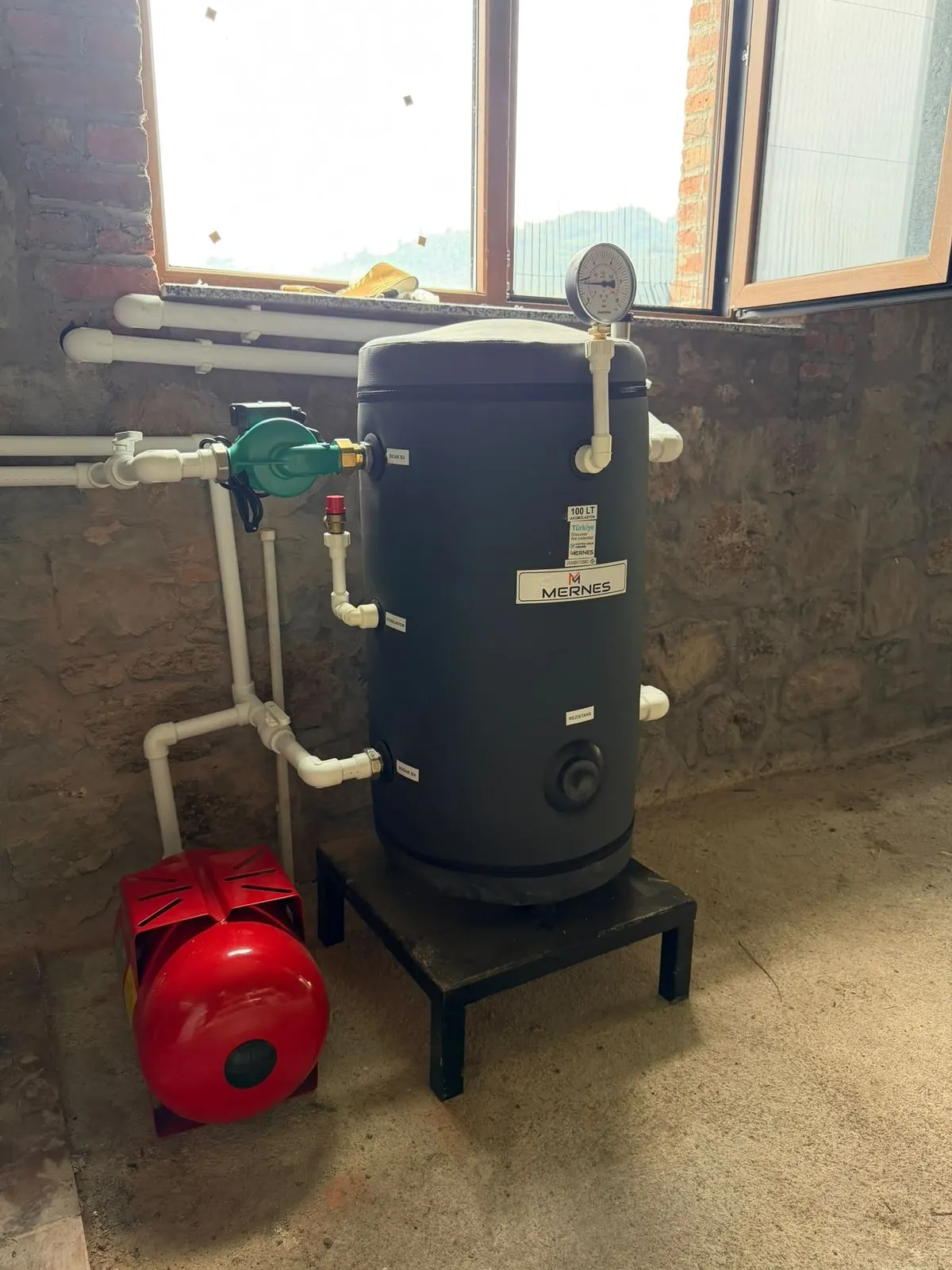 Taş duvarlı teknik odada boyler, kırmızı genleşme tankı ve pompa grubu